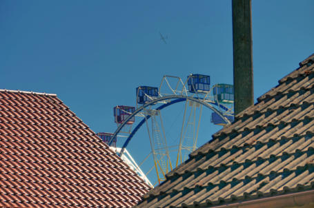 Zwischen den Dächern von Münsterhausen ragt ein Riesenrad in den blauen Himmel, auch ein Segelflieger ist mit von der Partie.